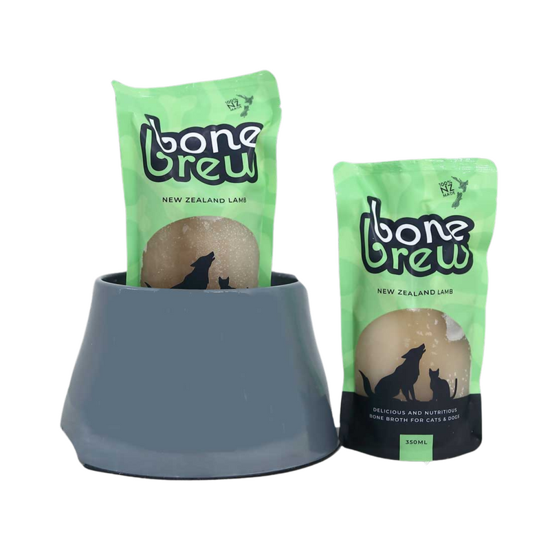 Two sealed pouches of Lamb Bone Broth by Bone Brew placed in a pet bowl, indicating the product is meant for pets.