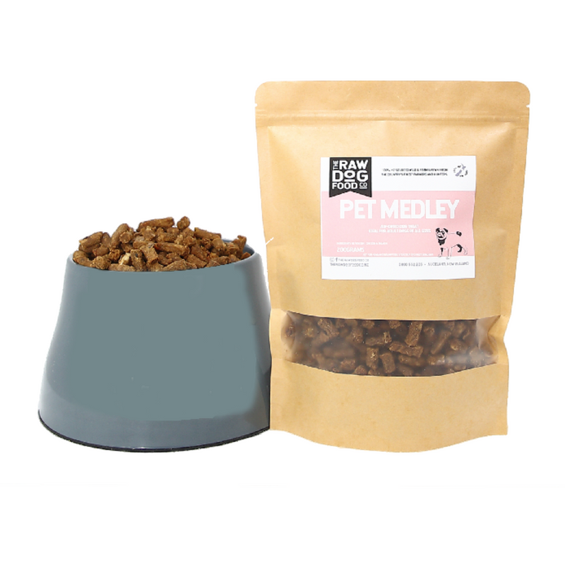 A package of air-dried dog treats next to a bowl filled with the same treats. The package is labeled 'Pet Medley' with images of venison, salmon, and chicken, indicating the flavors of the treats.