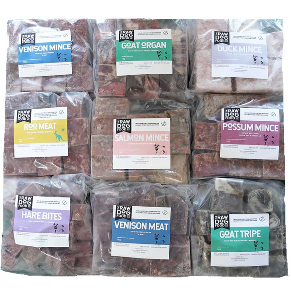Multiple sealed frozen packages of pet food with labels indicating different types such as 'VENISON MINCE', 'GOAT SRIGAN', and 'HARE MEAT'. The packages are part of a bulk box assortment.